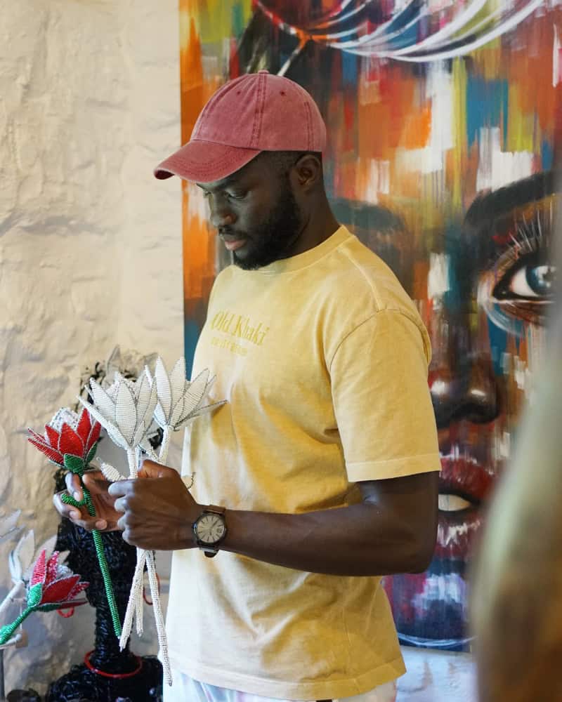 Tinashe Kachama holding a hand-beaded protea sculpture in pale pinks and creamy whites